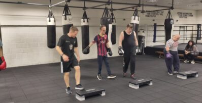 image shows a boxing coach helping some people to warm up