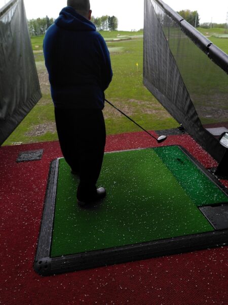 Image shows a man holding a golf club looking out at a driving range.